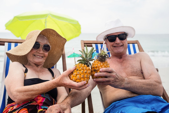 坐在沙滩椅上喝菠萝汁的老夫妇
