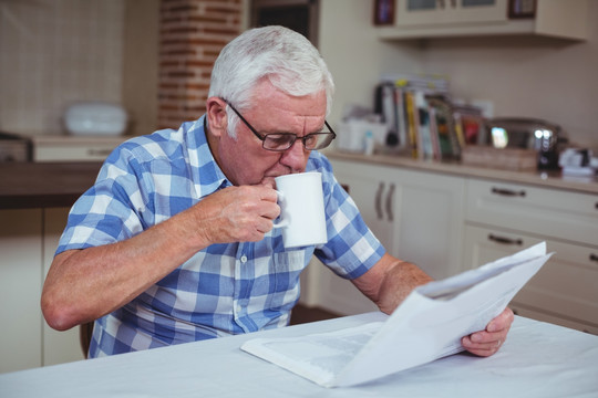 在厨房里看报纸喝咖啡的老人