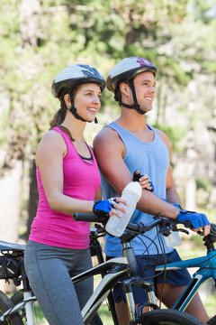 微笑的年轻夫妇在森林里骑自行车