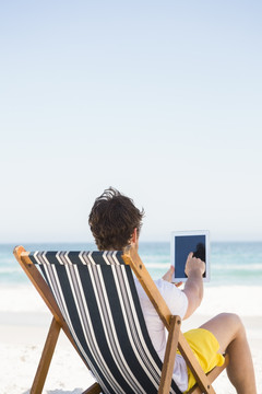 坐在海边使用平板电脑的男人