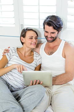 微笑的夫妇坐在床上使用平板电脑