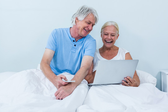 坐在床上使用笔记本电脑的老夫妇