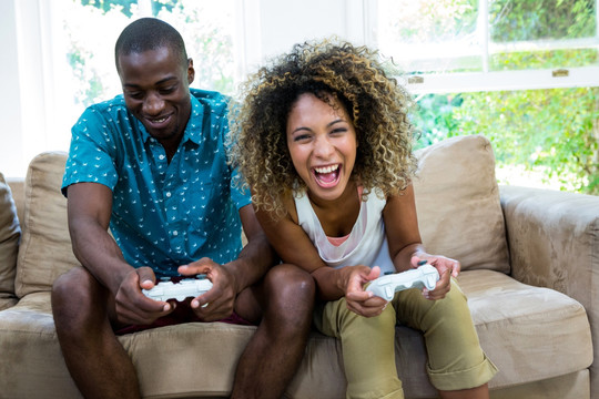 坐在沙发上玩电子游戏的年轻夫妇