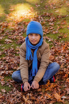 微笑的男孩坐在秋叶上