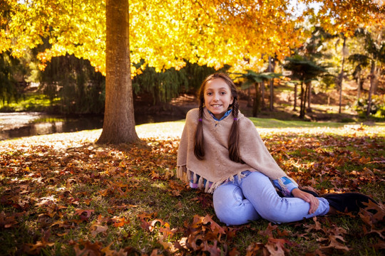 坐在秋天公园草坪上的女孩