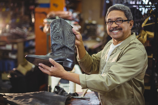 微笑在车间的鞋匠拿着皮靴的肖像