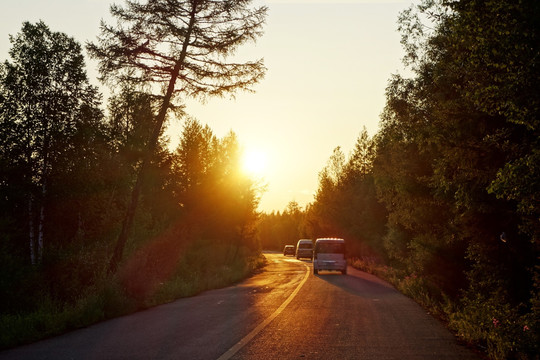 夕阳下森林公路行驶的车辆