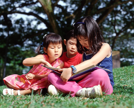 三个孩子坐在草地上看书