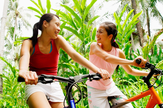 两个女孩骑着自行车穿过公园