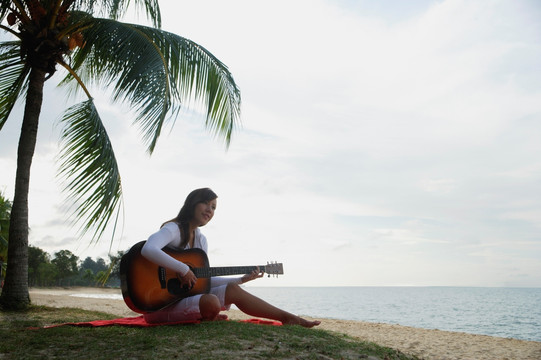 年轻女子坐在海滩上带着吉他