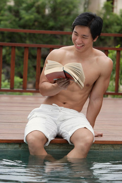 男子坐在游泳池边看书