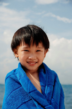 沙滩上裹着蓝色毛巾的小男孩