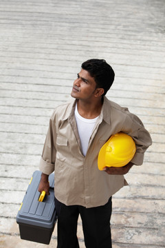 男子抱着建筑帽和工具箱望着远方