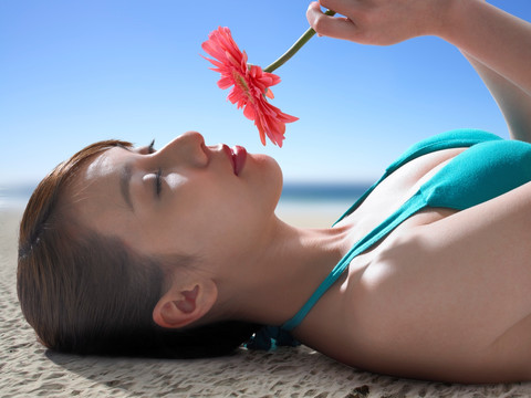 躺在沙滩上闻一朵花香的女人