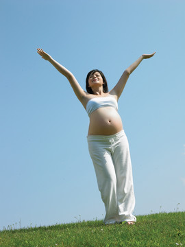 站在草坪上举起双臂的孕妇