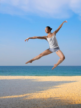 在海边张开双臂跳跃的女人