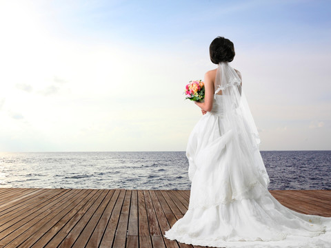 拿着一束花的新娘看着大海