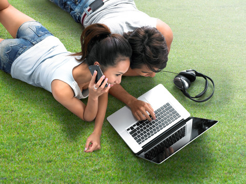 趴在草坪上用笔记本电脑的夫妇