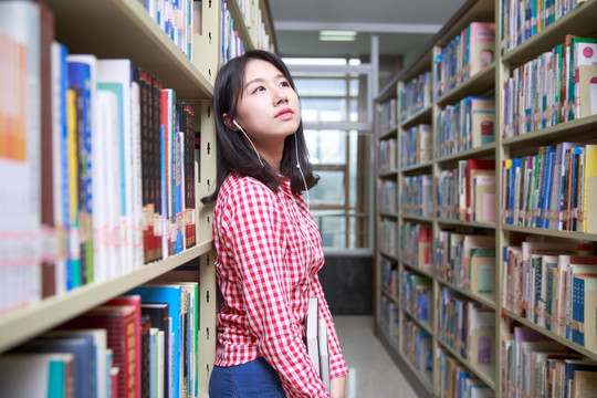 在大学图书馆里戴着耳机抬着头的女学生