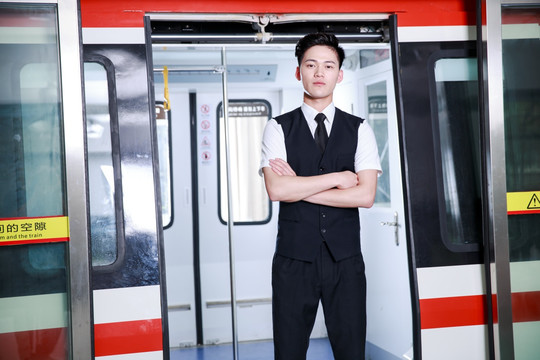 抱着双臂站在地铁门口的男乘务员