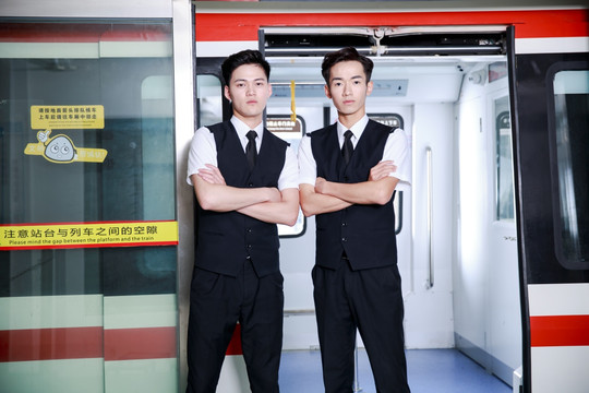 抱着双臂的两名男乘务员站在地铁门口