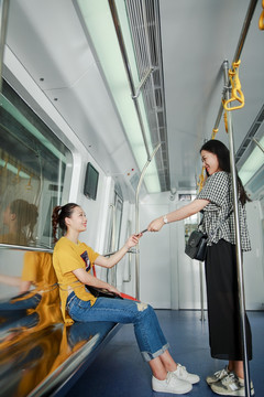 女人在地铁上把手机递给朋友