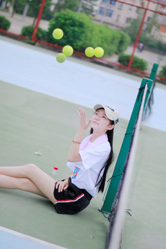 坐在球场地上抛网球的女大学生
