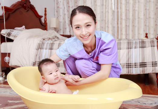 微笑的女家政员把婴儿放进洗澡盆里
