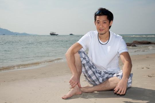 海边休闲装年轻男人坐在沙滩上