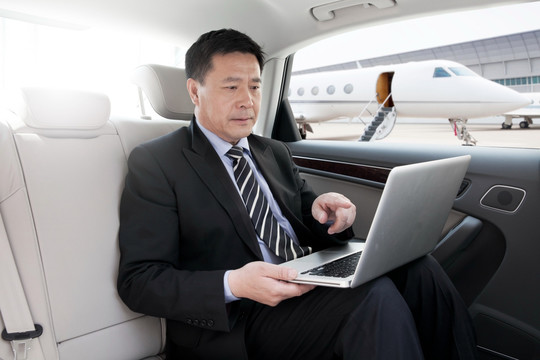 商务人士坐在轿车里使用笔记本电脑