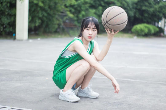 蹲在球场上单手拿着篮球的女学生