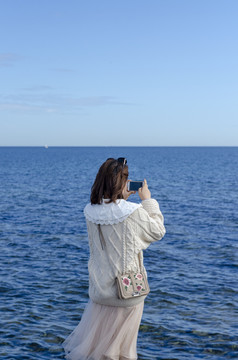 海边手机拍照的女孩背影