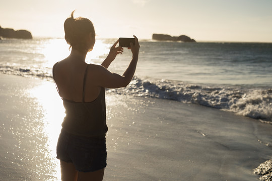 女运动员在沙滩上用手机拍照