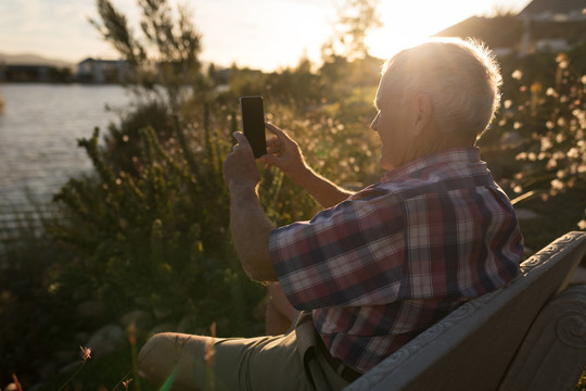 黄昏时分在河边用手机拍照的老人