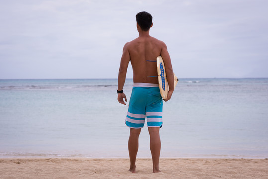 沙滩上站着冲浪板的人的后视图