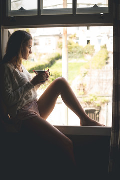 在阳台窗上喝咖啡的女人