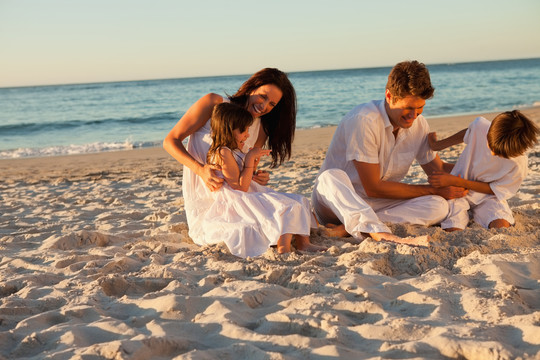 日落时坐在海滩上的一家人