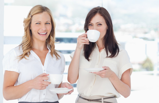 站在窗前喝咖啡的两个女白领