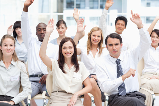 棕色头发的女人微笑着坐在抬起手臂的同事旁边。