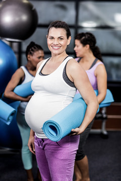 微笑的孕妇在休闲中心拿着运动垫