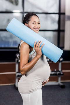 微笑的孕妇在休闲中心拿着运动垫
