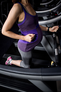 孕妇在健身房用跑步机触摸腹部