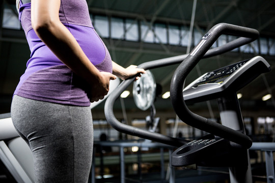 孕妇站在健身房的跑步机上