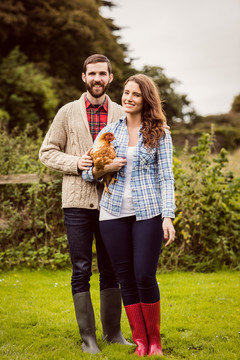 一对微笑的夫妇在乡下抱着鸡
