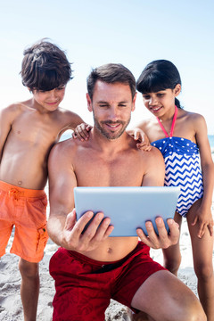 父亲和孩子在沙滩上使用平板电脑