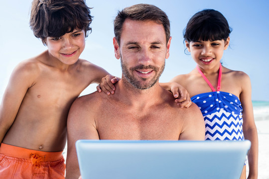 父亲和孩子在沙滩上使用平板电脑