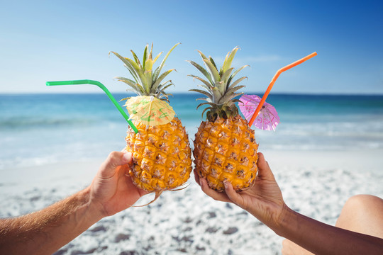 情侣在海滩上用菠萝鸡尾酒祝酒