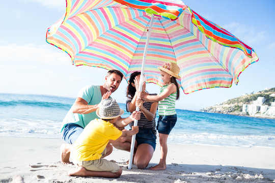 可爱的一家人把伞放在海滩上