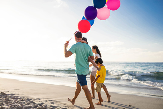 可爱的家庭在海滩上散步和拿气球