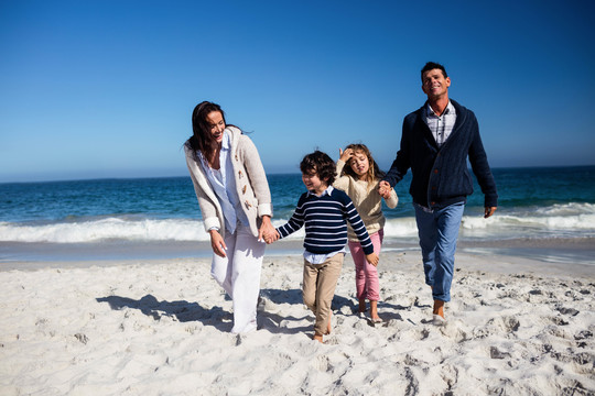 可爱的家庭牵着手走在沙滩上